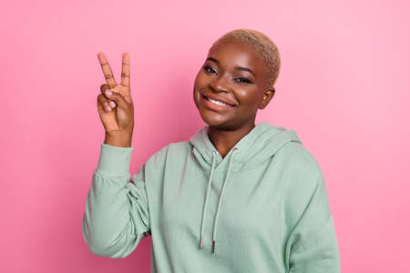 Photo of young adorable stunning lady with short hairstyle show v sign say hello isolated on pink...