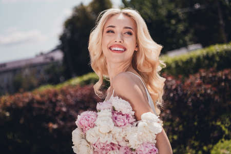Photo of funny dreamy young curly girl dressed white singlet enjoying sunny weather holding peonies outdoors countrysideの写真素材