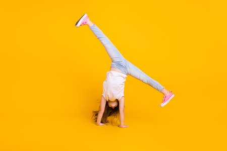 Full length photo of charming funny schoolgirl dressed white t-shirt walking hands upside down isolated yellow color backgroundの写真素材
