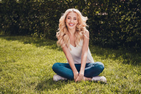 Photo of funny adorable young curly girl dressed white singlet sitting green grass enjoying sunny weather outdoors countrysideの写真素材
