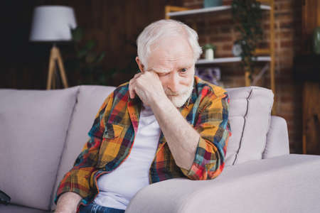 Photo of sad depressed man pensioner wear checkered shirt crying sitting sofa indoors house roomの写真素材
