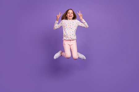 Full size photo of sportive active girl jumping arms fingers demonstrate v-sign isolated on violet...