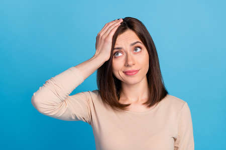 Portrait of unsatisfied person arm touch head look empty space isolated on blue color backgroundの写真素材