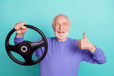 Photo of handsome aged man arm hold wheel demonstrate thumb up feedback isolated on turquoise color backgroundの写真素材