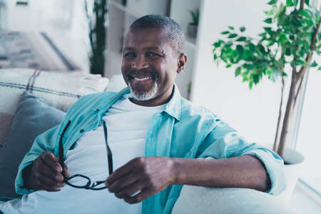 Photo of positive aged man agent hold specs choose new shopping advertisement optics sit divan in...