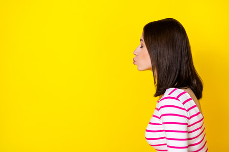 Profile photo portrait of winsome young lady lips kissing empty space dressed trendy striped clothes isolated on yellow color backgroundの写真素材