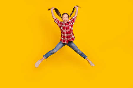 Photo of impressed pretty schoolkid dressed plaid shirt jumping high arms tails isolated yellow color backgroundの写真素材