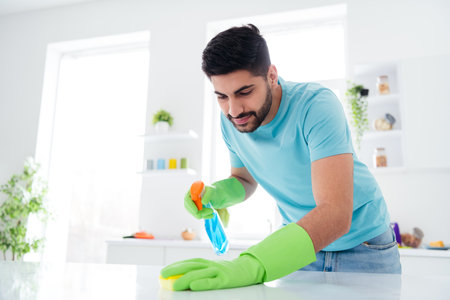 Portrait of neat young guy hold cleaning detergent bottle rag polishing table kitchen indoorsの写真素材