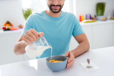 Cropped photo of young person hand hold pouring milk cornflakes plate breakfast kitchen house...