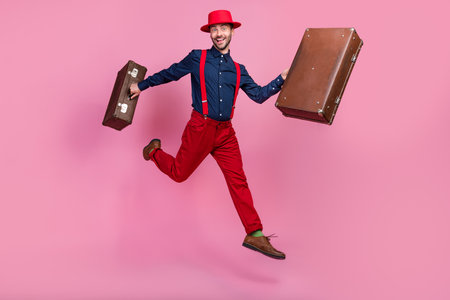 Full body size photo of young attractive handsome positive guy wear red suspenders hat costume run air hurry with bags holidays isolated on pink color backgroundの写真素材