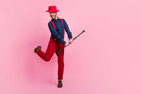 Full body portrait of cheerful carefree young man arms hold cane stick dancing isolated on pink color backgroundの写真素材