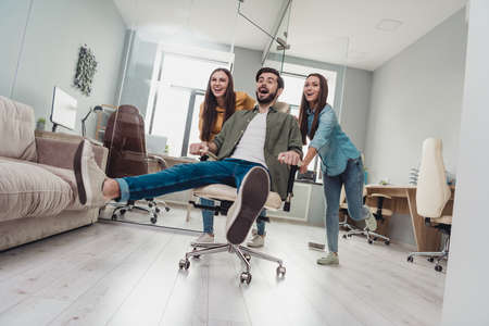 Full size photo of three overjoyed satisfied people playing enjoy pause break ride chair indoorsの写真素材