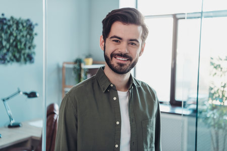 Portrait of attractive cheerful man wearing casual formal shirt developing project at work place station indoorsの写真素材