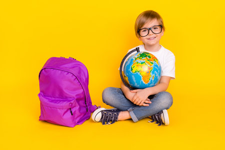 Portrait of handsome cheerful intellectual pre-teen boy holding supplies isolated over bright yellow color backgroundの写真素材