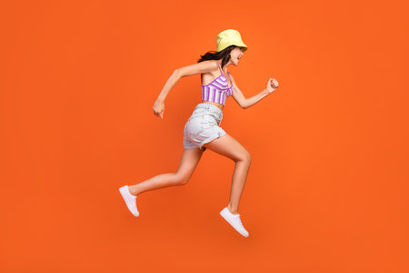 Full length photo of hurrying woman dressed violet bra jumping high running fast isolated orange color backgroundの写真素材