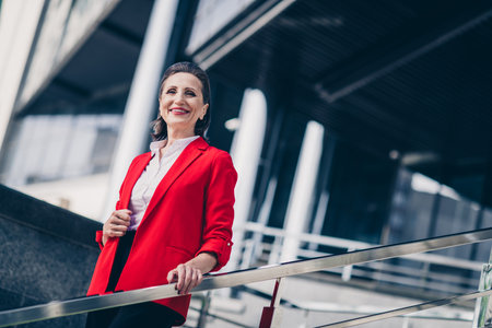 Photo of confident adorable senior advisor woman dressed red blazer smiling walking outdoors urban town streetの写真素材