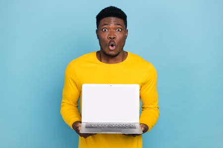 Photo of stunned guy hold new model laptop sale price offer wear long sleeve nice pullover isolated blue color backgroundの写真素材