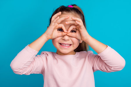 Photo of satisfied positive pupil arms fingers make eye binoculars isolated on blue color backgroundの写真素材
