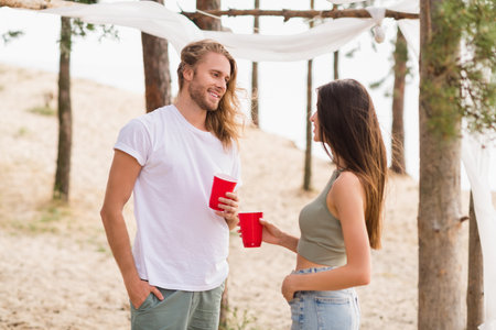 Portrait of lovely positive partners hold alcohol cups chatting communicate spend free time sand beach outsideの写真素材