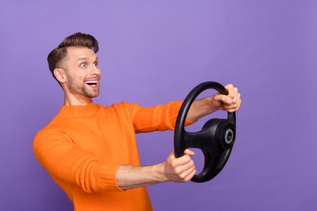 Photo of funky excited guy dressed orange pullover riding auto looking empty space isolated purple...