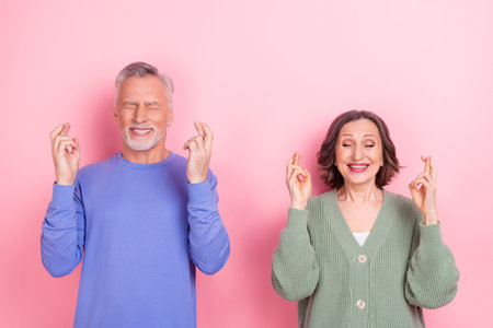 Portrait of two positive people closed eyes crossed fingers expect pray isolated on pink color backgroundの写真素材