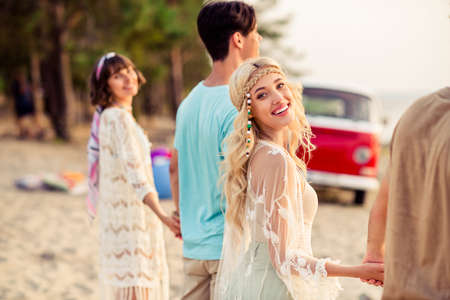 Photo of dreamy charming hippie people company smiling walking together holding arms outside seaside beachの写真素材