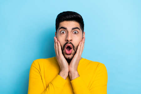 Photo of impressed handsome guy dressed yellow pullover arms cheeks isolated blue color backgroundの写真素材