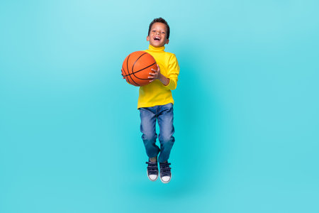 Full body portrait of active sportive boy jump hands hold basketball isolated on teal color...