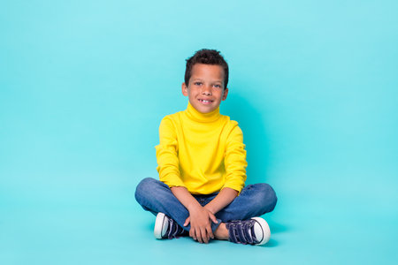 Full length portrait of satisfied schoolboy sit floor toothy smile isolated on turquoise color...