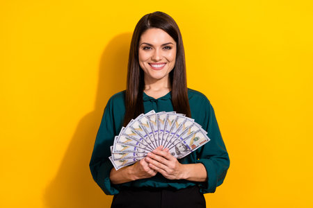 Photo of young pretty woman rich hold dollars earnings savings profit isolated over yellow color...