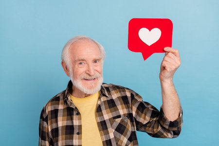 Photo of dreamy pretty man pensioner dressed checkered shirt holding heart like sign isolated blue...
