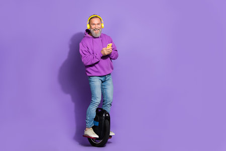 Photo of senior healthy cheerful man dressed purple hoodie on monowheel typing message smartphone...