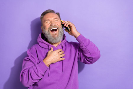 Photo of aged experienced attractive senior man hold phone talking laughter joke good mood empty space isolated on purple color backgroundの写真素材