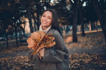 Photo of excited charming cheerful girl arms hold golden maple leaf toothy smile enjoy stroll...