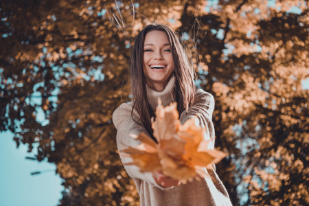 Photo of cheerful cute nice lady wear trendy cozy sweater hold dry leaves give you look camera beaming smile enjoy atmosphere outdoorsの写真素材