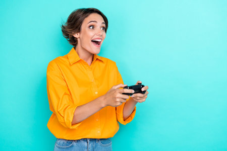 Portrait photo of young adorable pretty cute woman open mouth wear orange shirt surprised gamer excited isolated on cyan color backgroundの写真素材