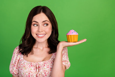 Photo of positive toothy beaming nice girl with wavy hairstyle wear blouse hold look at tasty cake isolated on green color backgroundの写真素材