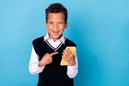 Photo of cheerful schoolkid indicate finger telephone application advert isolated on blue color backgroundの写真素材