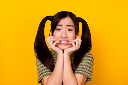 Portrait of young scared frightened loser girl bite her fingers have big problems isolated on yellow...