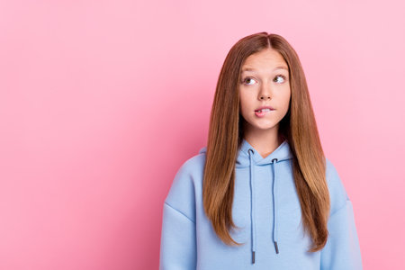 Portrait photo of young funny pretty little lady school learner wear blue hoodie bite lips dreamy look empty space advert wish isolated on pink color backgroundの写真素材