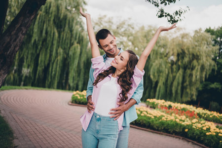 Photo of two idyllic positive partners cuddle hug raise hands enjoy each other walk outdoorsの写真素材