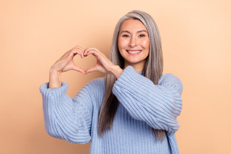 Photo of pretty shiny retired lady wear blue sweater showing arms heart isolated beige color backgroundの写真素材