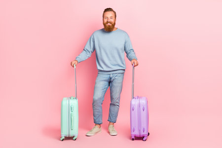 Full length portrait of cheerful nice person hold two suitcases isolated on pink color backgroundの写真素材