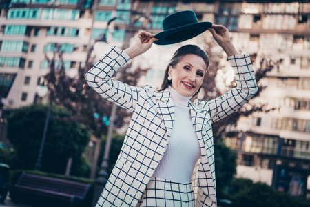 Photo of sweet charming lady dressed checkered blazer rising cap walking sunny weather outdoors urban town streetの写真素材