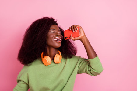 Photo of adorable sweet lady wear green sweater earphones singing mic modern gadget empty space isolated pink color backgroundの写真素材