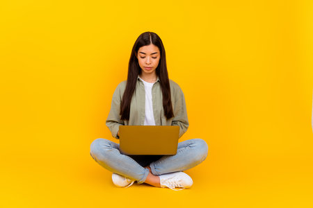 Full length photo of serious focused young lady sit floor use wireless netbook isolated on yellow color backgroundの写真素材