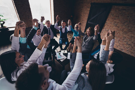 Portrait of delighted group business people sitting chair hold raise hands success achievement office indoorsの写真素材