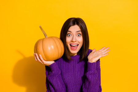 Portrait of cheerful impressed girl hand hold pumpkin open mouth toothy smile isolated on yellow color backgroundの写真素材