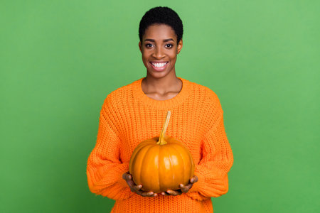 Photo of pretty young short hairdo guy hold pumpkin wear orange sweater isolated on green color backgroundの写真素材