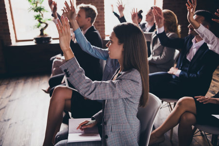 Businesspeople at event listening to presenter studying rising hands asking at loft wood brick industrial style interior indoorsの写真素材